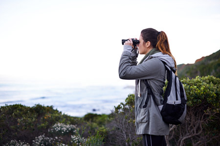 Woman, mountain and binoculars in nature environment for trekking hike for holiday, explore or...