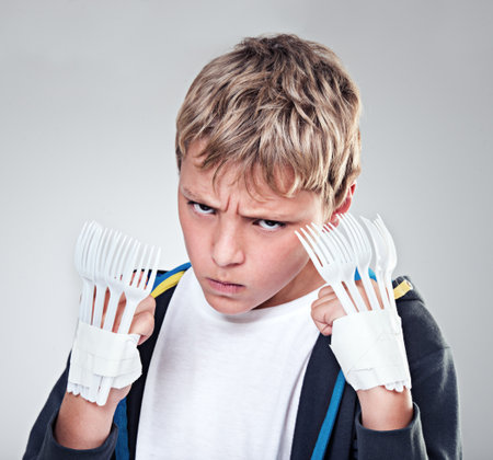 Portrait, angry and boy with fist, fight and expression with frustrated on grey studio background. Face, model and kid with forks for claws and reaction with costume and aggressive with rage or childの写真素材