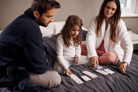 Mom, dad and girl with playing cards to relax in home with bonding, learning or fun with strategy in bedroom. Father, mother and daughter with games, maths or teaching with connection in family houseの写真素材