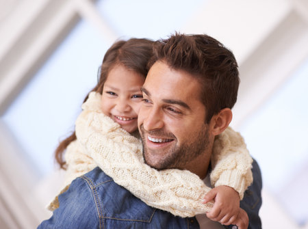 Happy, hug and piggyback for child from dad in home on holiday or relax with family on vacation. Father, love and support girl on back for funny game, bonding and playing together on weekendの写真素材