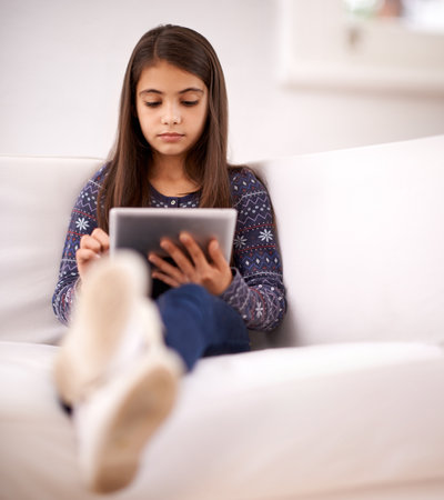 Relax, sofa or girl with tablet for elearning, playing games or streaming videos on a movie website. Education, online or child in home with technology to download on app or reading ebook on couchの写真素材
