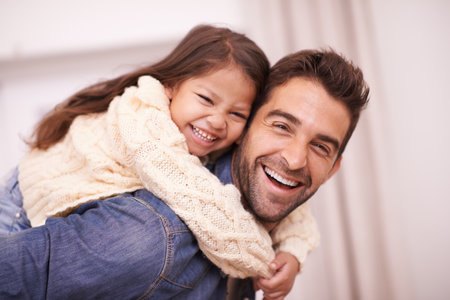 Happy, portrait and child piggyback on dad in home on holiday or relax with family on vacation. Hug, father and support girl on back with love for funny game, bonding and playing together on weekendの写真素材