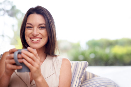 Woman, home and smile in couch with tea to relax or chill on break, day off and enjoy. Portrait, female person and happy in living room on sofa with cup of coffee for rest and calm in lounge.の写真素材
