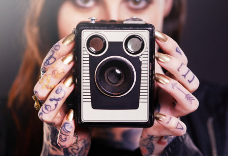Tattoo, portrait or woman with retro camera in studio for hobby, creative photography or memory. Closeup, vintage technology or photographer with ink on hands or picture device on black backgroundの写真素材