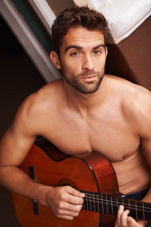 Portrait, home and guitar with man, topless and training with talent or sound with musician. Face, person or apartment with guy or string instrument for practice or confidence with hobby or shirtlessの写真素材