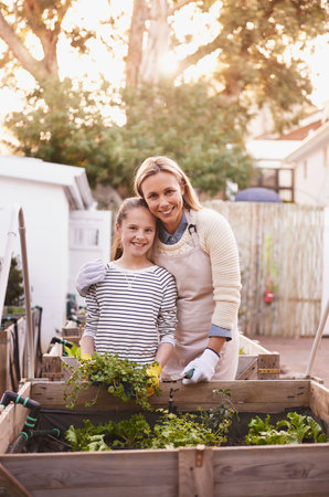 Mother, daughter and gardening with portrait in home for bonding, happy family and organic hobby. Woman, girl child and smile with sustainability, agriculture and plant growth in backyard of houseの写真素材