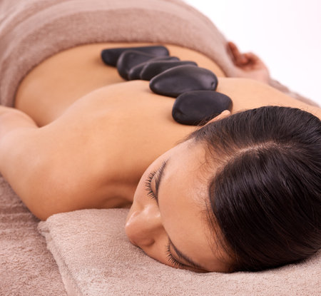 Wellness, hot stone and woman with back massage at spa for health, self care and grooming treatment in studio. Skin, calm and person with masseuse for warm rock body routine by white background.の写真素材