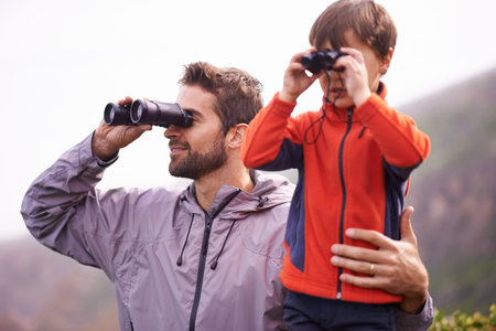Dad, kid and binoculars with smile from hiking, travel and watching in nature with adventure. Parent, youth and father with love, support and trust outdoor with family with view on trip with walkingの写真素材