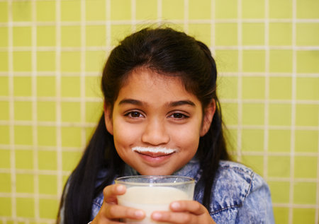 Milk moustache, smile or girl portrait in house with healthy breakfast drink on yellow wall background. Protein, dairy and face of kid in india with milkshake for balance, energy or calcium nutritionの写真素材