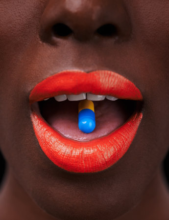 Black woman, lipstick and pill in mouth for health, beauty supplement and bright makeup color on dark background. Collagen, medicine and tablet for cosmetic care with closeup of orange lip balmの写真素材