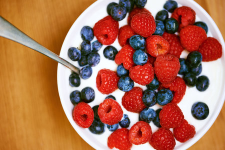 High angle, berries and nutrition with yogurt, raspberry and blueberry for organic snack. Food, cuisine and breakfast for health, wellness and diet for morning bowl or antioxidant wellbeing in studioの写真素材