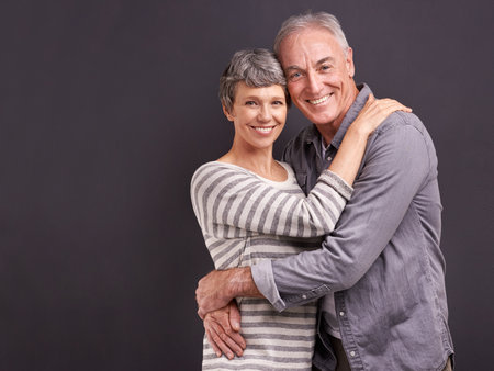 Portrait, hug and old couple with love, smile and relationship on a grey studio background. Retirement, happiness or senior man with mature woman or embrace with romance, marriage or bonding togetherの写真素材
