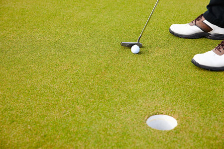 Feet, club and golf ball for hole on field, training and practice for competition or tournament. Closeup, shoes and target for outdoor challenge and exercise, person and professional athlete on lawnの写真素材