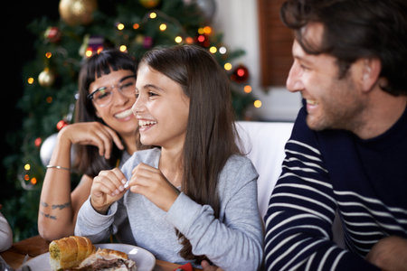 Christmas, family and happy parents with child in home for dinner, lunch and eating together. Mother, father and girl laughing with food for holiday, vacation and festive celebration at dining tableの写真素材