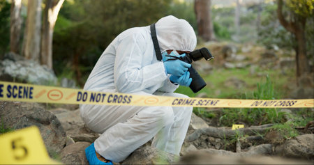 Forensic, photographer and police tape at crime scene for investigation in forest with evidence and safety hazmat..Csi quarantine, expert investigator and pictures for observation and case researchの写真素材