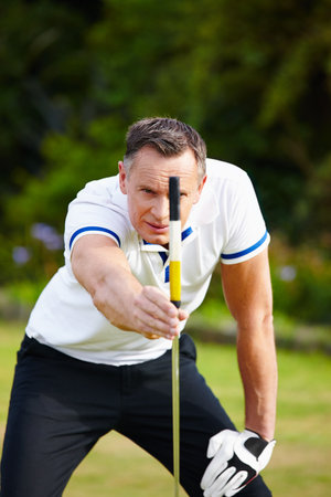 Man, golf and club with grass for aim for putt with strategy for skill in sportswear on course. Male person, health and fit with sport with equipment, mature and healthy in outdoors with accuracyの写真素材