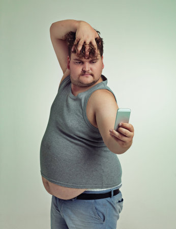 Selfie, cellphone and plus size man in studio posing with casual, trendy and cool outfit with...