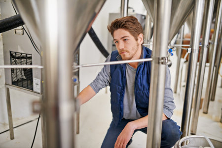 Brewery, production and man with steel in factory or distillery for winery, alcohol and drink manufacturing. Worker or winemaker checking container, metal or pipe of fermentation vessel for beerの写真素材