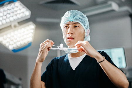 Medical, uniform and doctor in theatre for surgery, safety and preparation for operation in hospital. Asian man, surgeon and clothes with thinking for cardiology procedure, protection and healthcareの写真素材