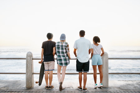 Sunrise, fashion and back of friends by ocean for holiday, summer vacation and weekend outdoors. Diversity, promenade and men and women by seaside for travel, adventure and relax together for bondingの写真素材