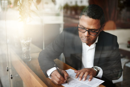 Businessman, corporate document and writing in cafe for attorney contract, legal paperwork and glasses. Lawyer, person and review for insurance claim, investment policy and remote work by windowの写真素材