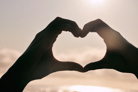 Silhouette, heart hands and couple at beach for sunset, love and bonding for care together on summer holiday. Shadow, closeup and romance at ocean sea for peace, support and emoji sign for connectionの写真素材