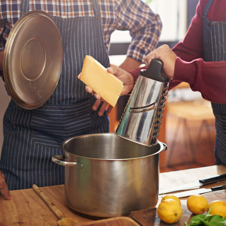 Person, hands and cooking with pot for cheese or diary dish in kitchen or secret recipe together at home. Closeup of friends, team or people in hospitality or mixing ingredients with apron at houseの写真素材