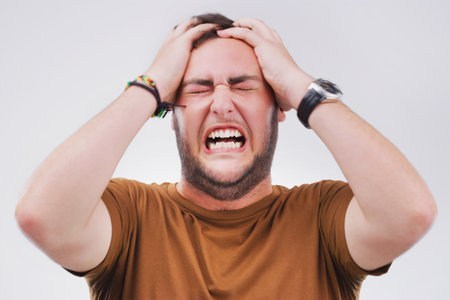 Anger, burnout and frustration with annoyed man in studio isolated on gray background for reaction. Emotion, rage and stress for fail with young person feeling upset at accident, fail or mistakeの写真素材