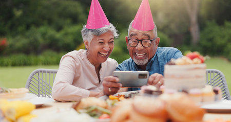 Elderly, couple and happy with video call at birthday party for celebration, laughing and memories in garden. Senior, man and woman with smartphone for photography, gathering and event in backyardの写真素材