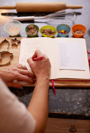 Hands, kitchen and writing in book for recipe in countertop for dinner, seasoning and flavor at home. Person, ingredients and notebook with menu in table for cooking method and prepare for mealの写真素材