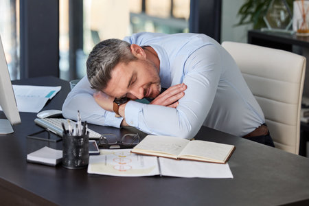 Tired, business man and sleeping at desk in office with resting, nap or burnout from working on report. Exhausted, professional and male employee for fatigue, deadline stress or snooze in workplaceの写真素材