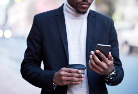 Black businessman, fashion and hands with smartphone and coffee for connection, travel or work break. Formal, male person and technology with drink for commute to workplace with communicationの写真素材