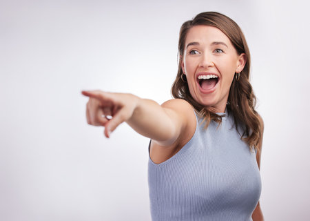 Woman, excited and pointing in direction with news, announcement and surprise isolated on white background. Information, about us and wow reaction with crazy opportunity, coming soon and attentionの写真素材