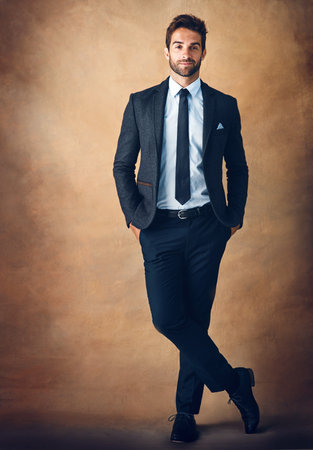 Studio, portrait and man with corporate fashion, confidence or business professional in studio. Gentleman, trendy style and businessman on brown background with pride, opportunity or designer clothesの写真素材