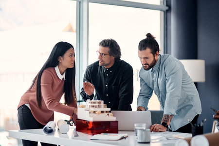 Architect, team and meeting with laptop for planning, discussion or design for construction at office. Group of creative employees or civil engineers brainstorming on computer for building or startupの写真素材