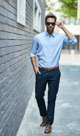 Confident, man and wall in street with sunglasses for fashion, style and trendy in outdoor. Male person, pride and fashionable in town for work, corporate or career in mens wear in city backgroundの写真素材