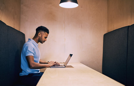 Businessman, typing and research with laptop in office cubicle for online browsing, communication or email. Young man or creative employee working or reading on computer for news, feedback or startupの写真素材