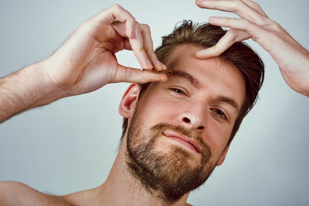 Man, portrait and tweezer for grooming, eyebrows and pluck in hygiene, routine or treatment. Male person, white background and hair removal for wellness, skincare and mockup space or beauty in studioの写真素材