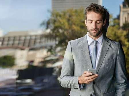 Corporate, confidence and businessman on balcony with smartphone for networking, reading email or news. Lens flare, professional and person with mobile for texting, browsing internet or social mediaの写真素材