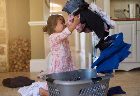 Girl, child and home or laundry with throw or basket, mischief and cleaning with attitude. Kid, job or tantrum with washing in house and messy, bad behaviour and untidy with clothes for familyの写真素材