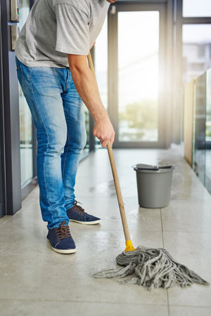 Janitor, mop and clean floor in office for routine maintenance, cleanliness and sanitation in workspace. Washing tiles, person and ground staff in company for spill, disinfection and hygieneの写真素材