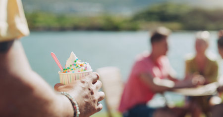 Person, ice cream and cup outside for eat with plastic spoon at lake for fresh air in summer. Dessert, cold and sweet at park in Germany with vacation or weekend in sunshine with tasty snack.の写真素材