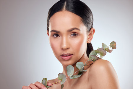 Girl, portrait and plant for skincare in studio, facial treatment and sustainable cosmetics. Female person, leaves and eco friendly product to pamper skin, organic dermatology and gray backgroundの写真素材