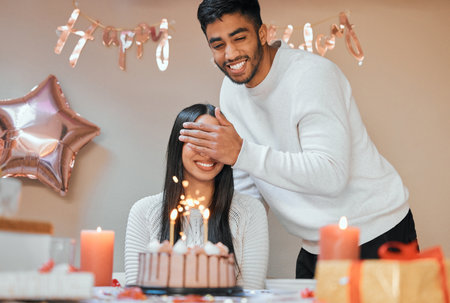 Couple, surprise and candles on cake for birthday, celebration and pride in apartment for life event. Man, woman and smile for party with happiness at table for love, gift and partnership in homeの写真素材