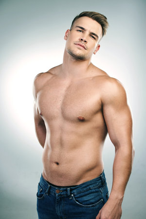 Portrait of man, abs and shirtless in studio with jeans for confidence, physical training or workout results on white background. Body, strong and model for bodybuilder, muscles or transformationの写真素材