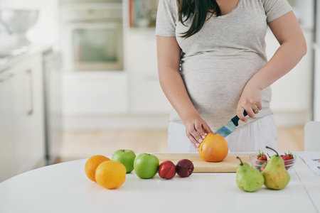 Woman, pregnant and cutting fruit in home, nutrition and vitamin for growth of baby. Female person, organic and vegan snack or hands for health, cooking and healthy diet for maternity in kitchenの写真素材