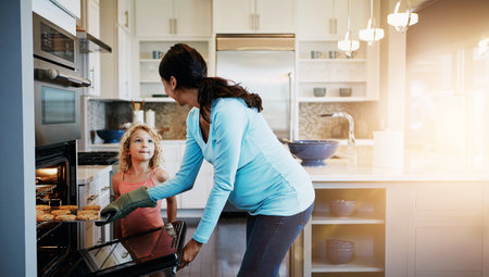 Mother, daughter and cookies in oven for baking in kitchen with learning, bonding and fun in home with sunlight. Family, woman and girl with cooking dessert, cake and sweet snack by stove in houseの写真素材
