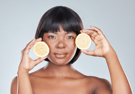 Skincare, portrait or black woman in studio with lemon for wellness, shine or dermatology glow treatment on grey background. Face, cleaning or girl model with fruit for citrus, benefits or skin detoxの写真素材