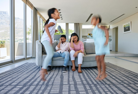 Parents, jump and stress in home, kids and tired with anxiety, burnout and noise in a living room. Mother, father and energetic children in a lounge, fatigue and depressed or motion and headacheの写真素材