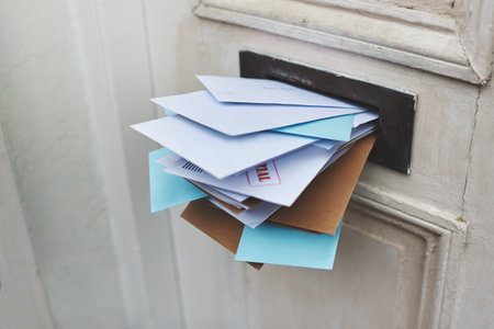 Door, letter and mail or envelope in box of home for communication or notice, stacked and overflowing with documents. Mailbox, post and address for mortgage or debt, message and paper from bank.の写真素材